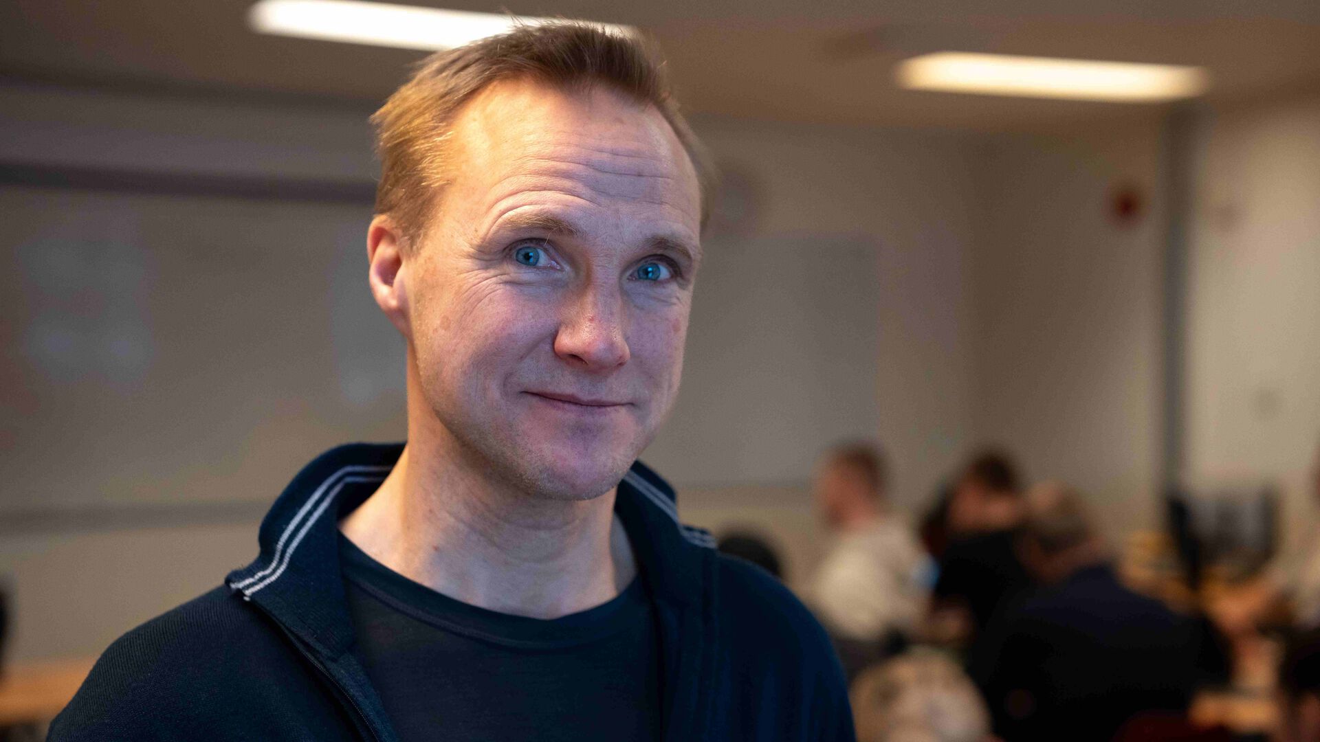 Tormod Heir ser i kamera i et klasserom, studenter diffust i bakgrunnen