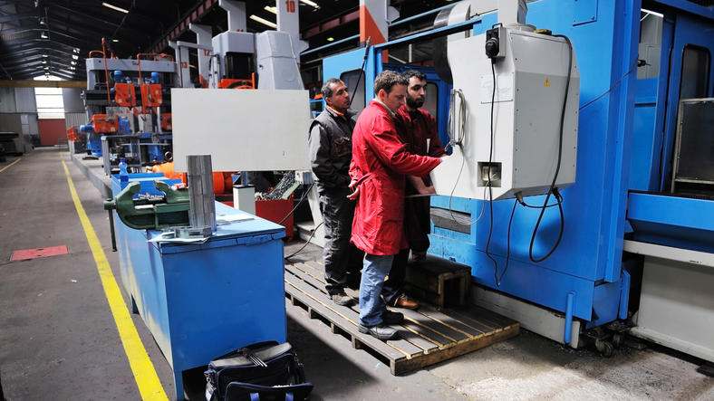 Bilde av tre innvandrere som jobber ved en maskin i en fabrikk
