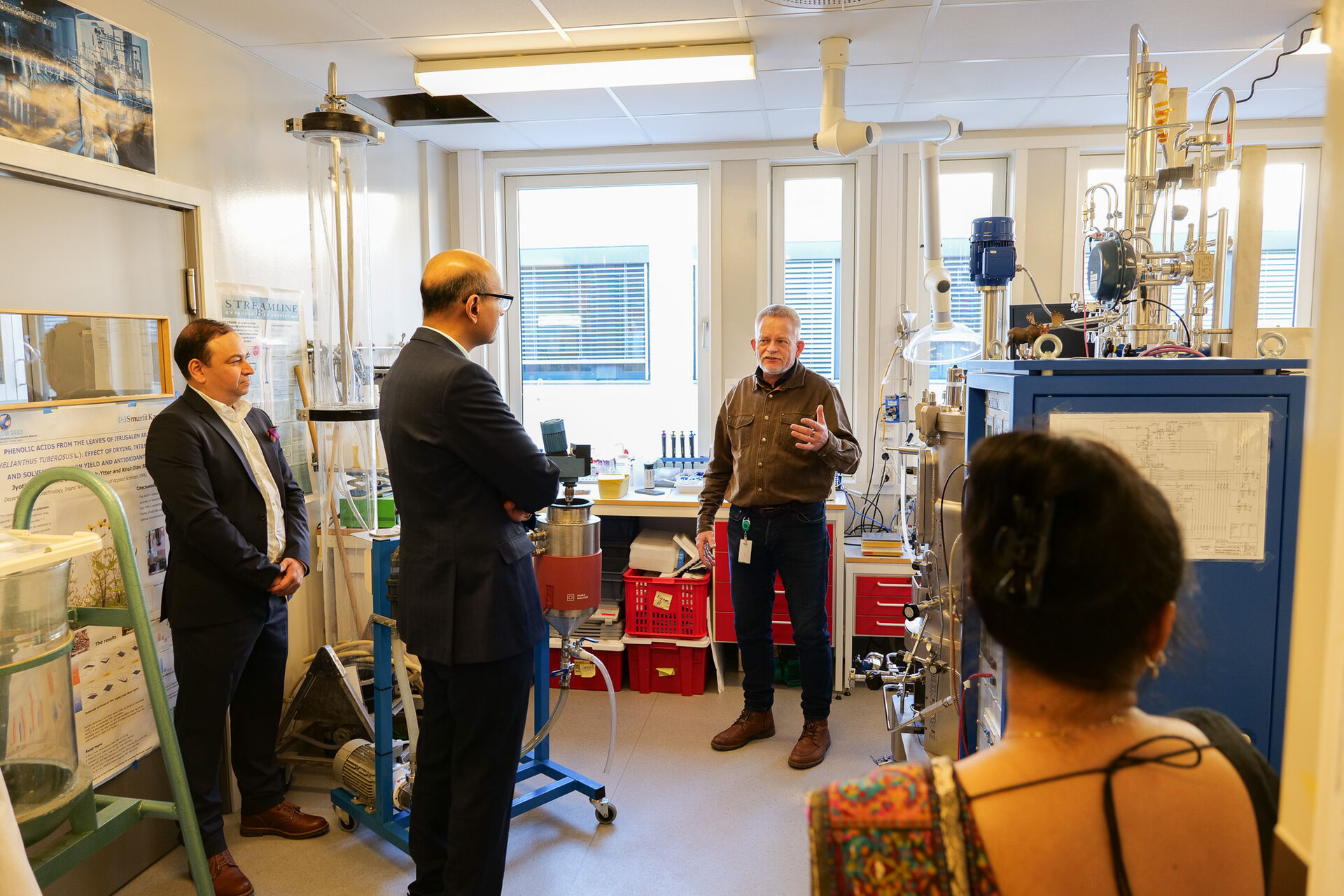Fire mennesker står inne på et bioteknologilaboratorium, en forteller, andre hører på.