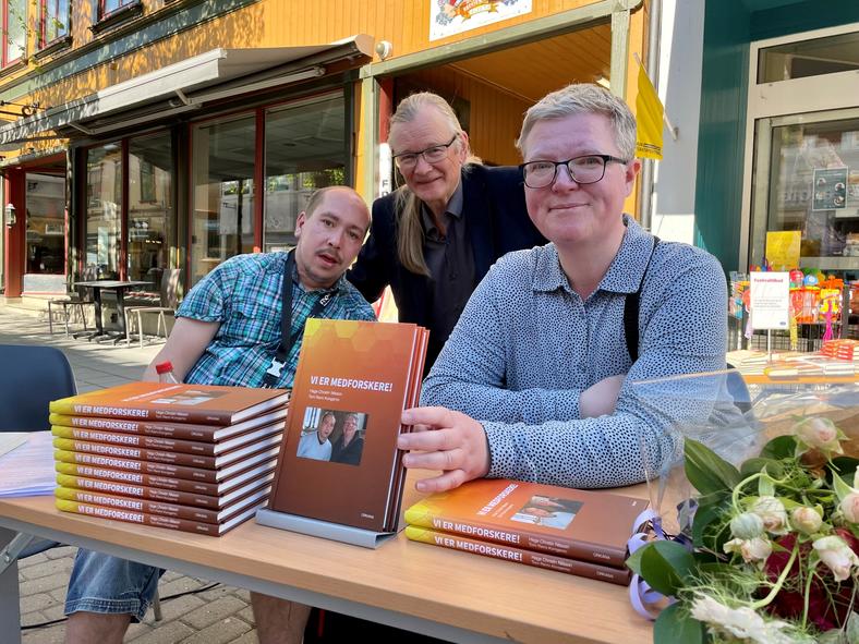 Tre forfattere ved et bord på ei gate