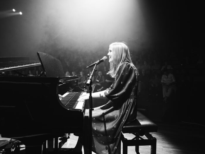 Ingunn Listuen is sitting by the piano on the stage while performing. 