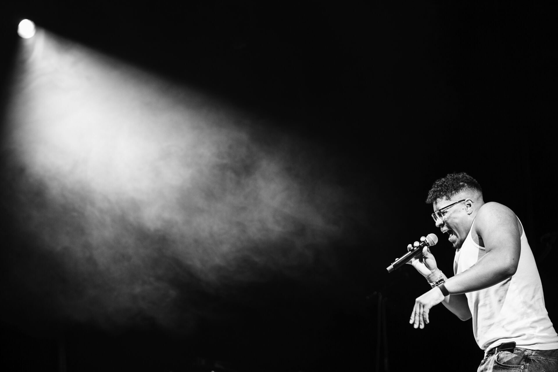 A male student is singing. We see him from the left side. On the top left we see stage lights.