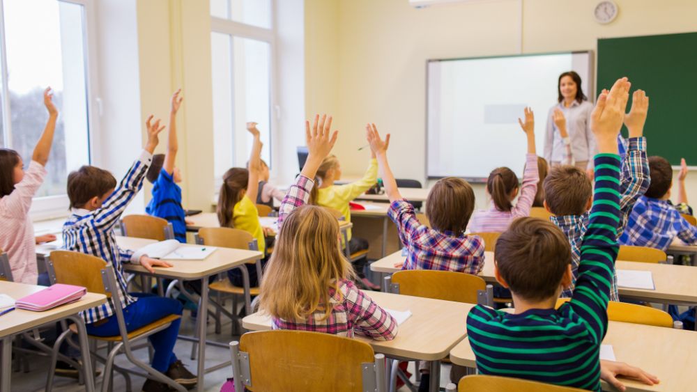 Bilde av barn i et klasserom som rekker opp hendene