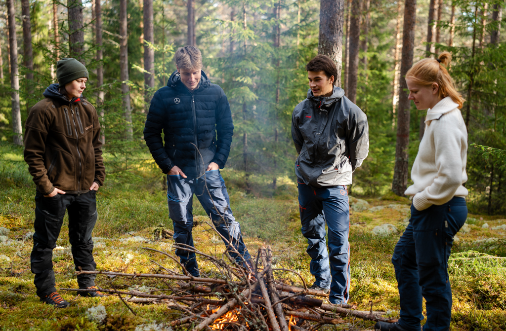 A group of four students are standing around the fire