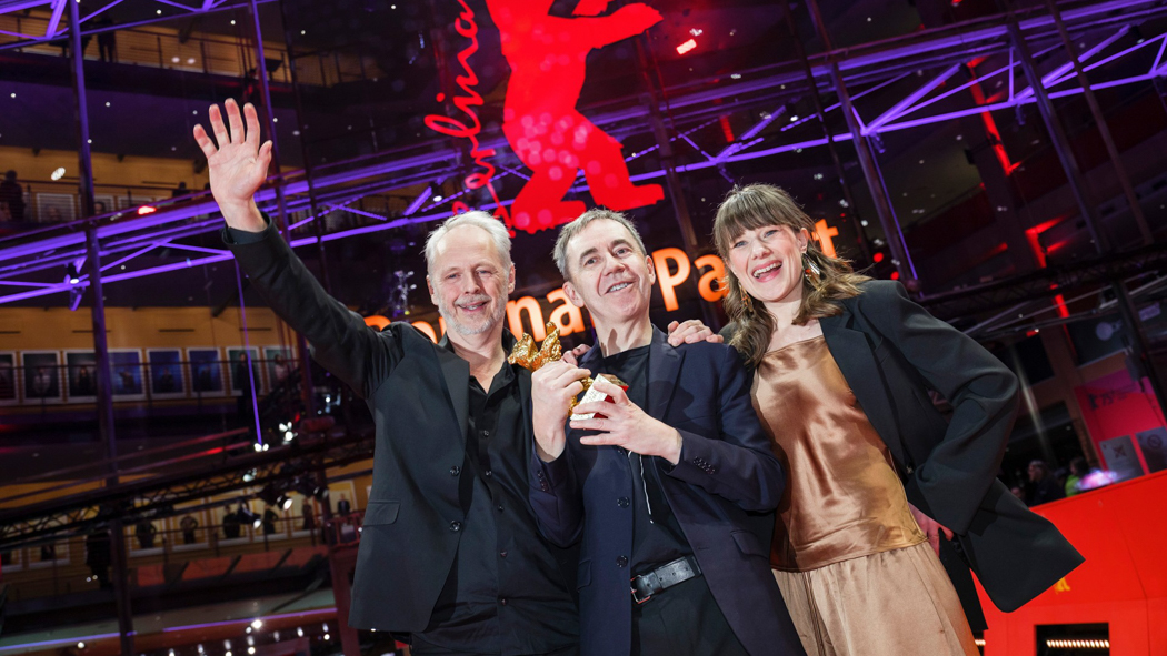 Regissør og to produsenter med Gullbjørn-statuetten foran Berlinale-logo 