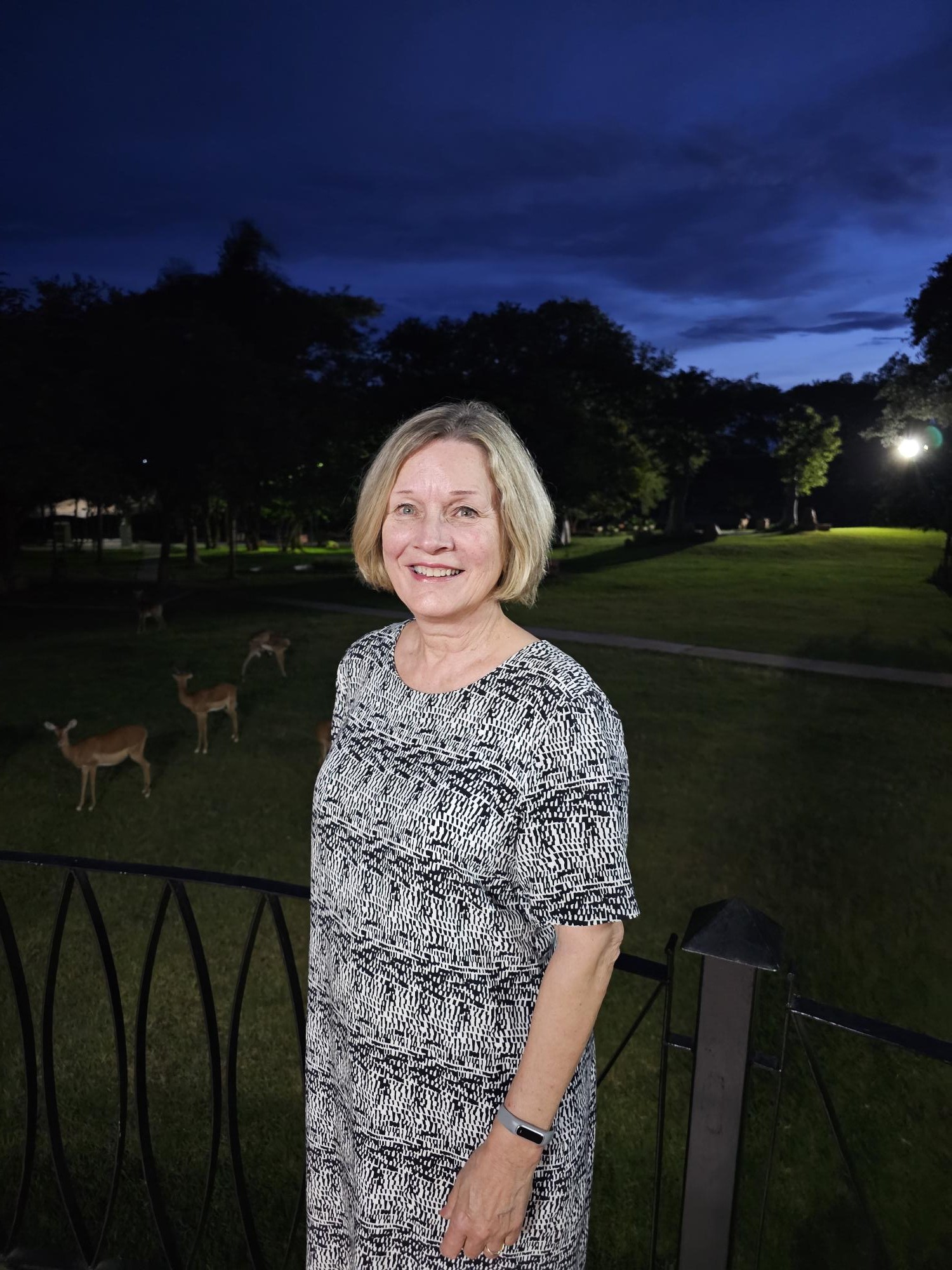 Anne Marit Danbolt på en terrasse, det er mørkt, men noen impalaer skimtes i bakgrunnen. 