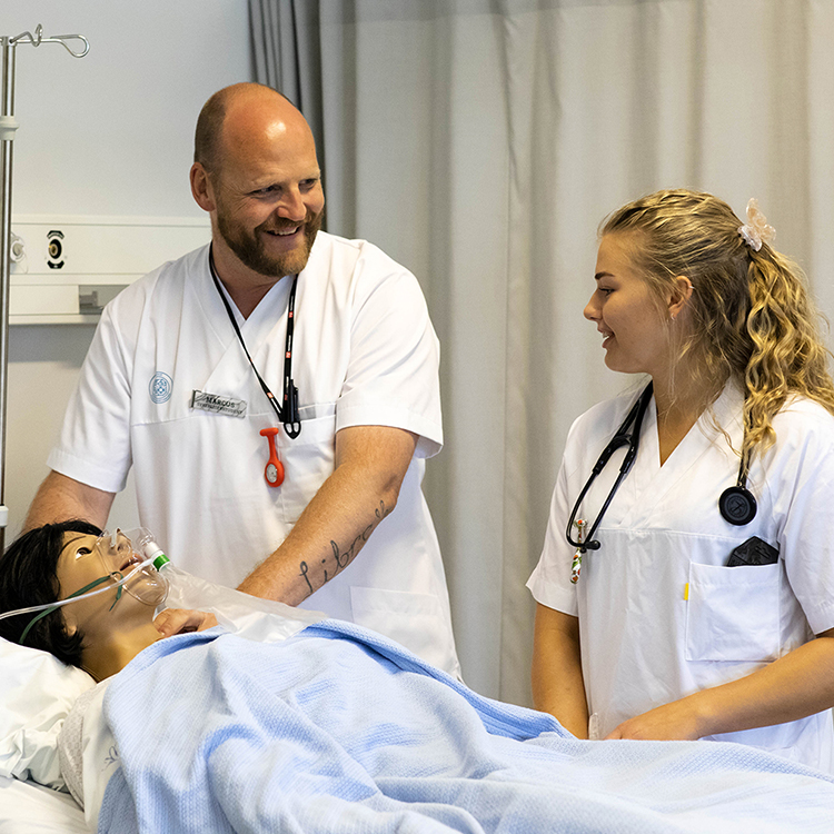 To smilende sykepleiestudenter som jobber på en dukke. 