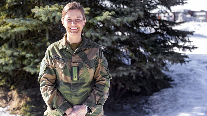 Bilde av en offiser kledd i grønn uniform foran et grønt tre. 