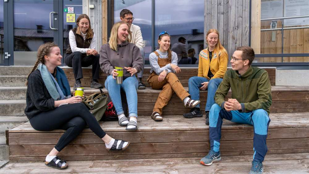 Seks studenter sitter på en trapp utenfor inngang til campus Evenstad.