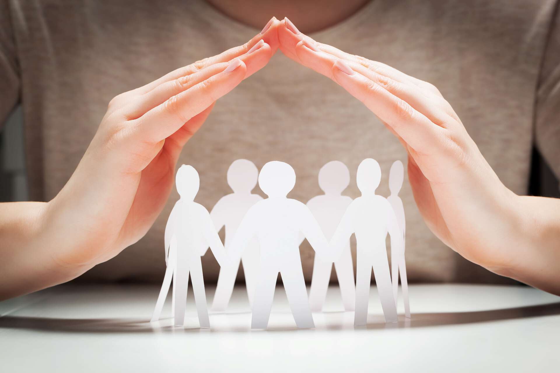 Hender former et beskyttende tak over en gruppe papirfigurer som symboliserer familie eller fellesskap.