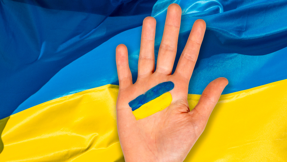 En åpen hånd med påmalte striper i blått og gult som i det ukrainske flagget, ligger oppå et ukrainsk flagg