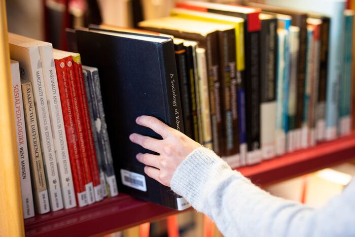 Hånd som tar bok ut fra bokhylle