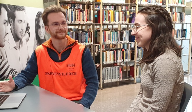 A male student wearing a vest labeled 'writing guide'. Next to him sits a female student.