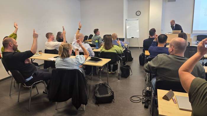 Klasserom sett bakfra, hvor mange av studentene rekker hånden i været.