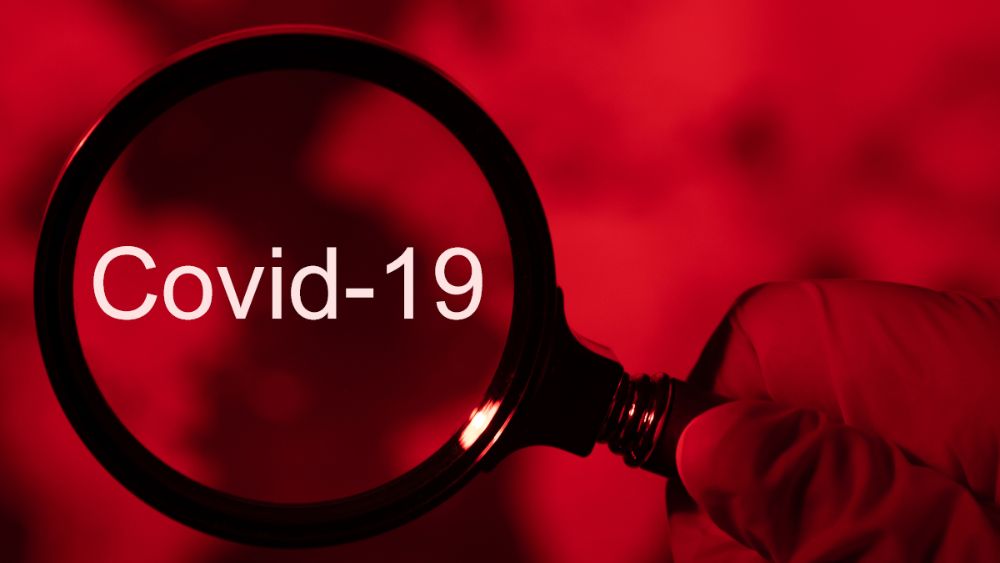 Covid-19 text with a magnifying glass over it with a red background.