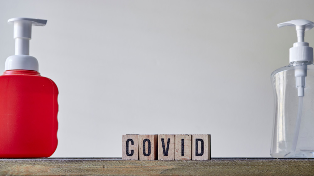 Wooden cubes with letters forming the word COVID between two hand sanitizer bottles.