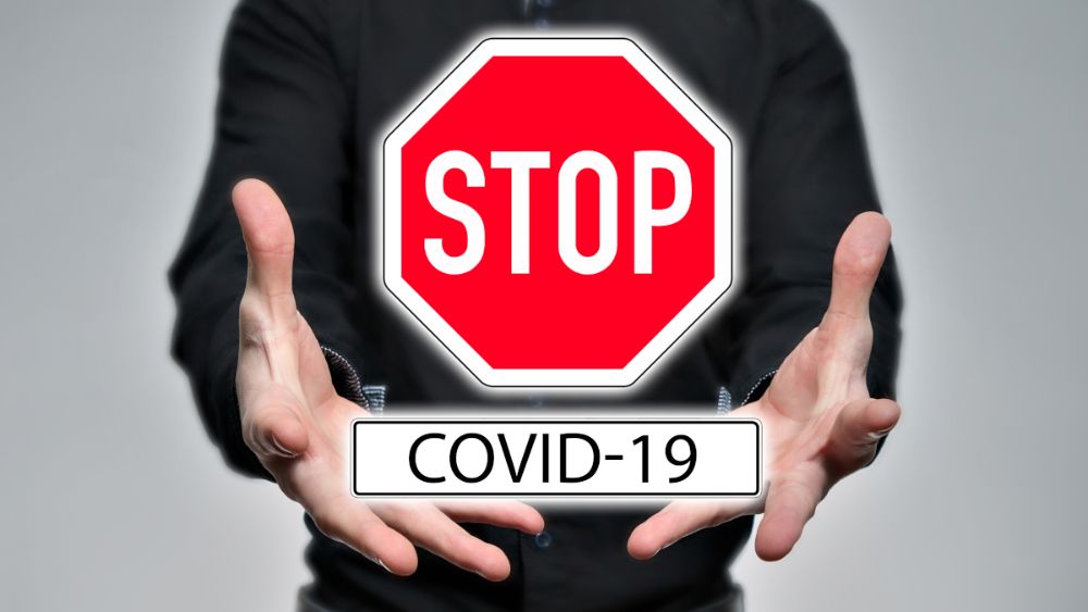 A person holding a sign with the text STOP COVID-19