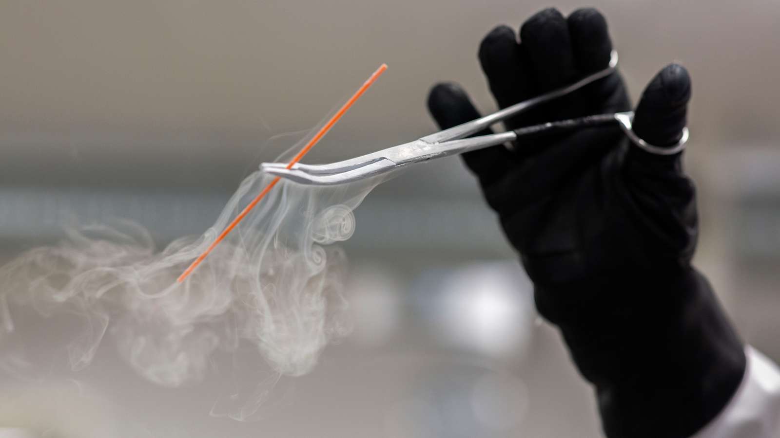 A gloved hand holding up a deep-frozen thread of bull semen.