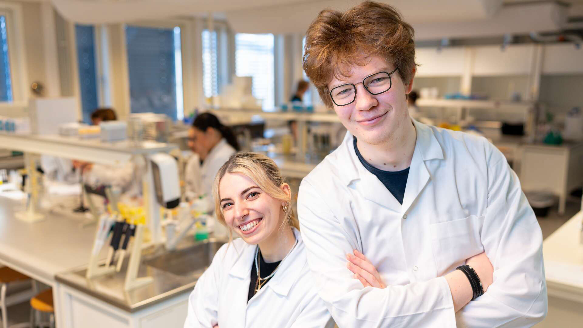 Two students are smiling at the camera in a lab