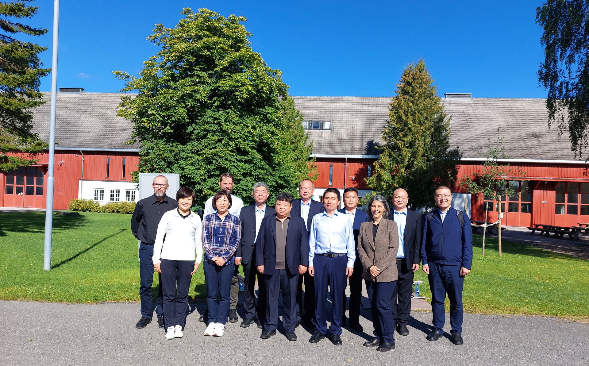 Employees from HINN and the Chinese delegation standing in front of the barn. In the background you can see green trees.