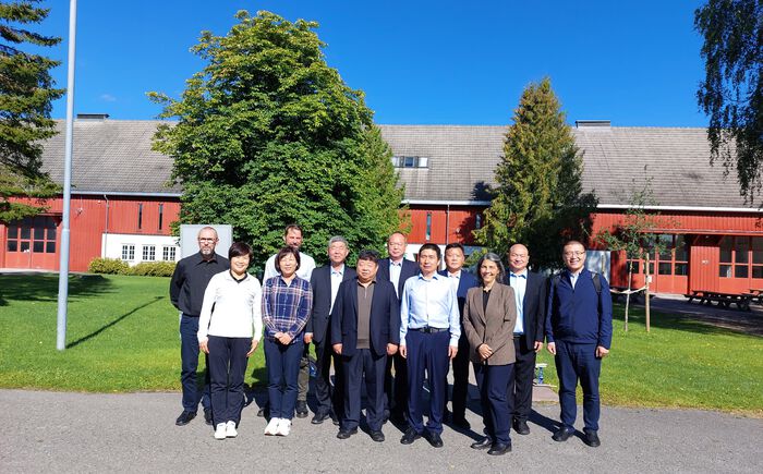Employees from HINN and the Chinese delegation standing in front of the barn. In the background you can see green trees.