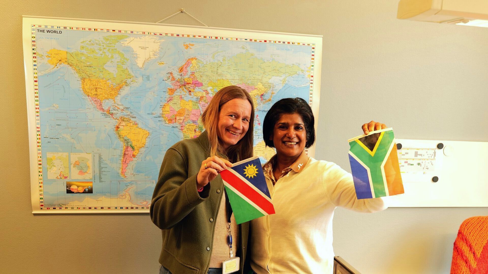 To kvinner står foran et verdenskart og holder flagg fra Namibia og Sør-Afrika