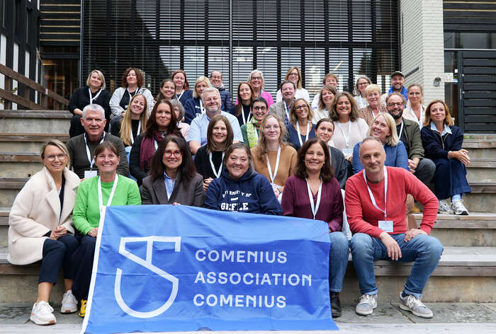 A group of Comenius Association representatives gathered on the steps at INN University, holding a blue Comenius Association banner