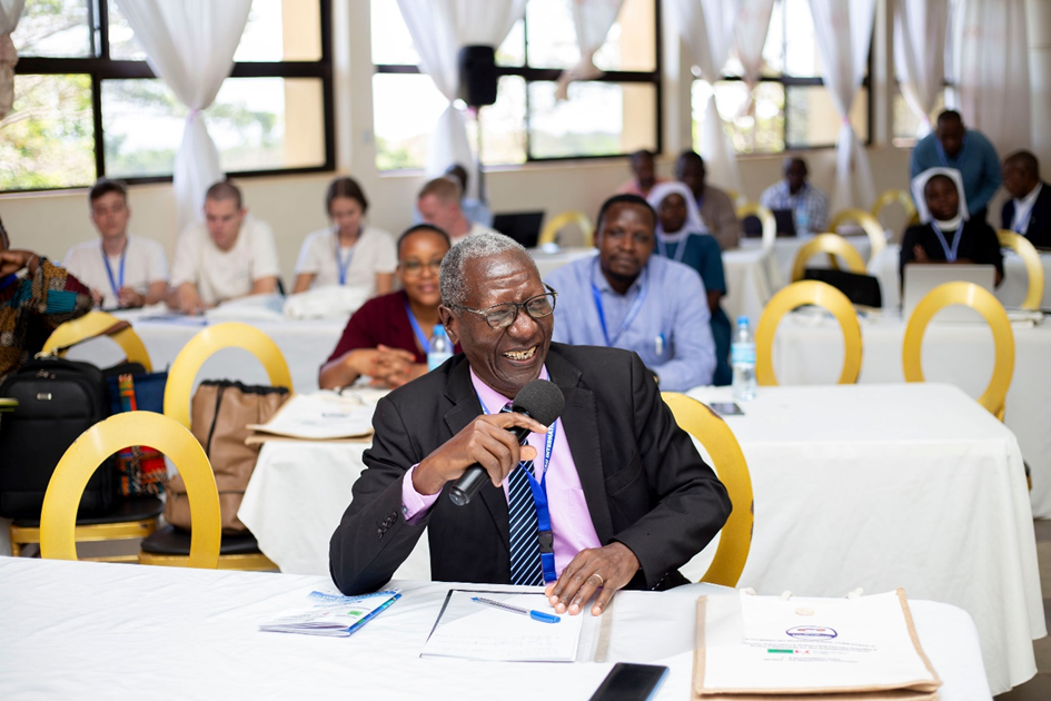 Didas Kimaro is sitting at a table and speaking at the conference
