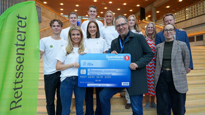 A group of smiling people with a large check in front of them standing on a large staircase.