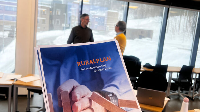 Brochure in blue and orange about RURALPLAN project, in the blurry background are two men talking