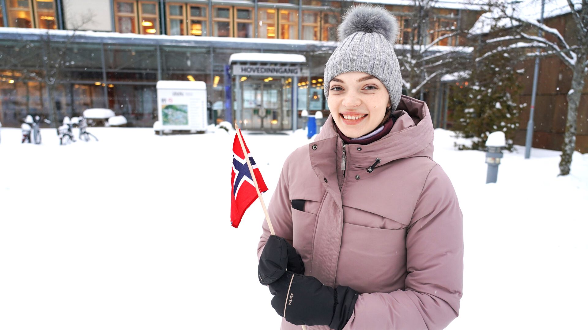 Portrait of Yuliia Myroshnychenko outside in the snow. She's holding a Norwegian flag in front of Lillehammer campus
