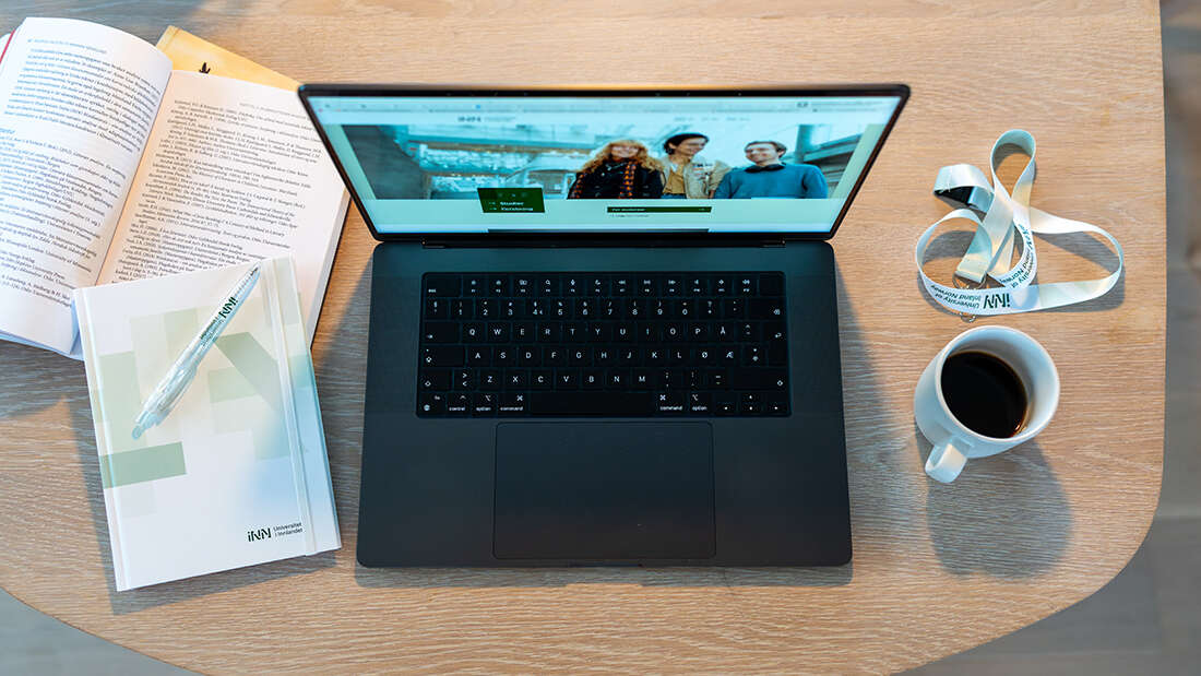 A table with a coffee cup, acomputer screen and a notepad.
