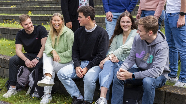 A group of happy students are sitting outside of Lillehammer campus on a sunny day.