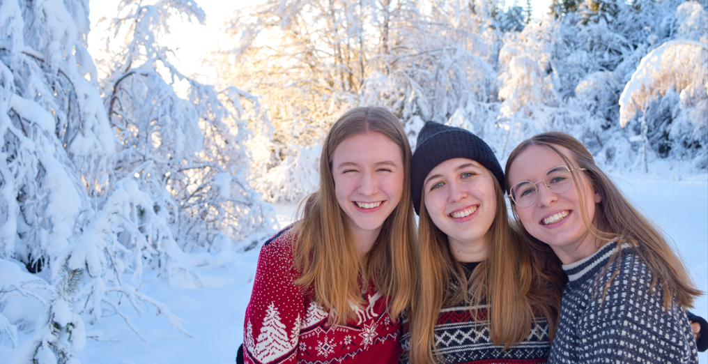 Female exchange students dressed in woollen sweaters posing in the snow covered forest.