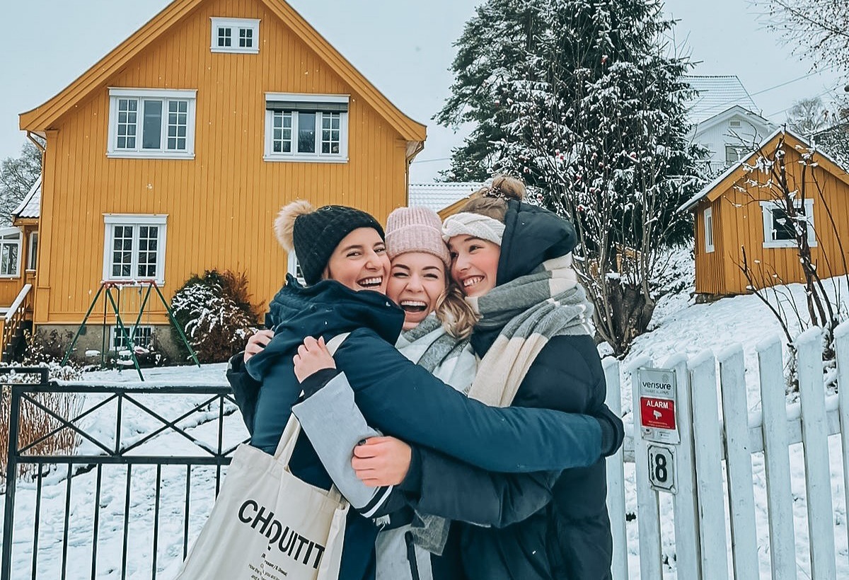 Female students hugging in front of a yellow house and snow covered entry during winter