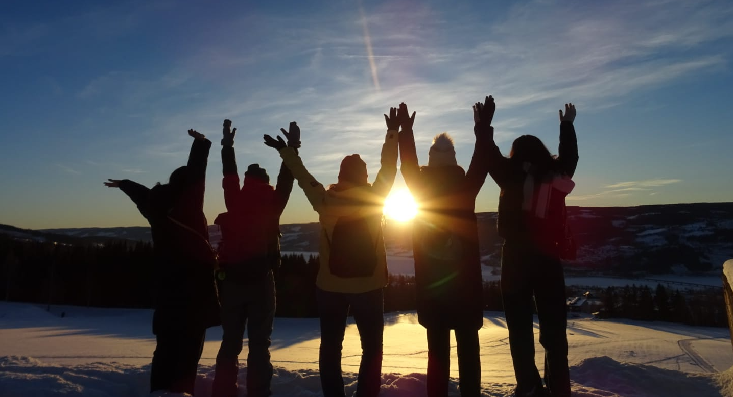 Exchange students posing with their backs, looking at the sunset, holding hands raised up.