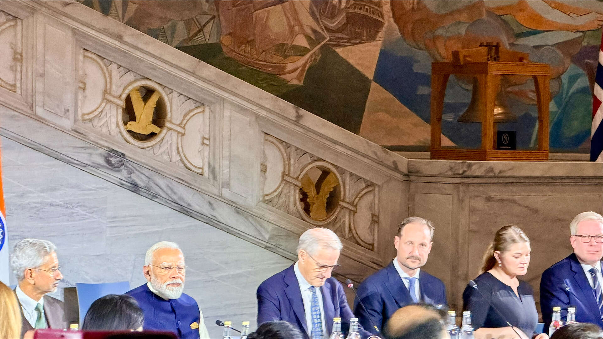 Five men and one woman seated at a long table at an official event.