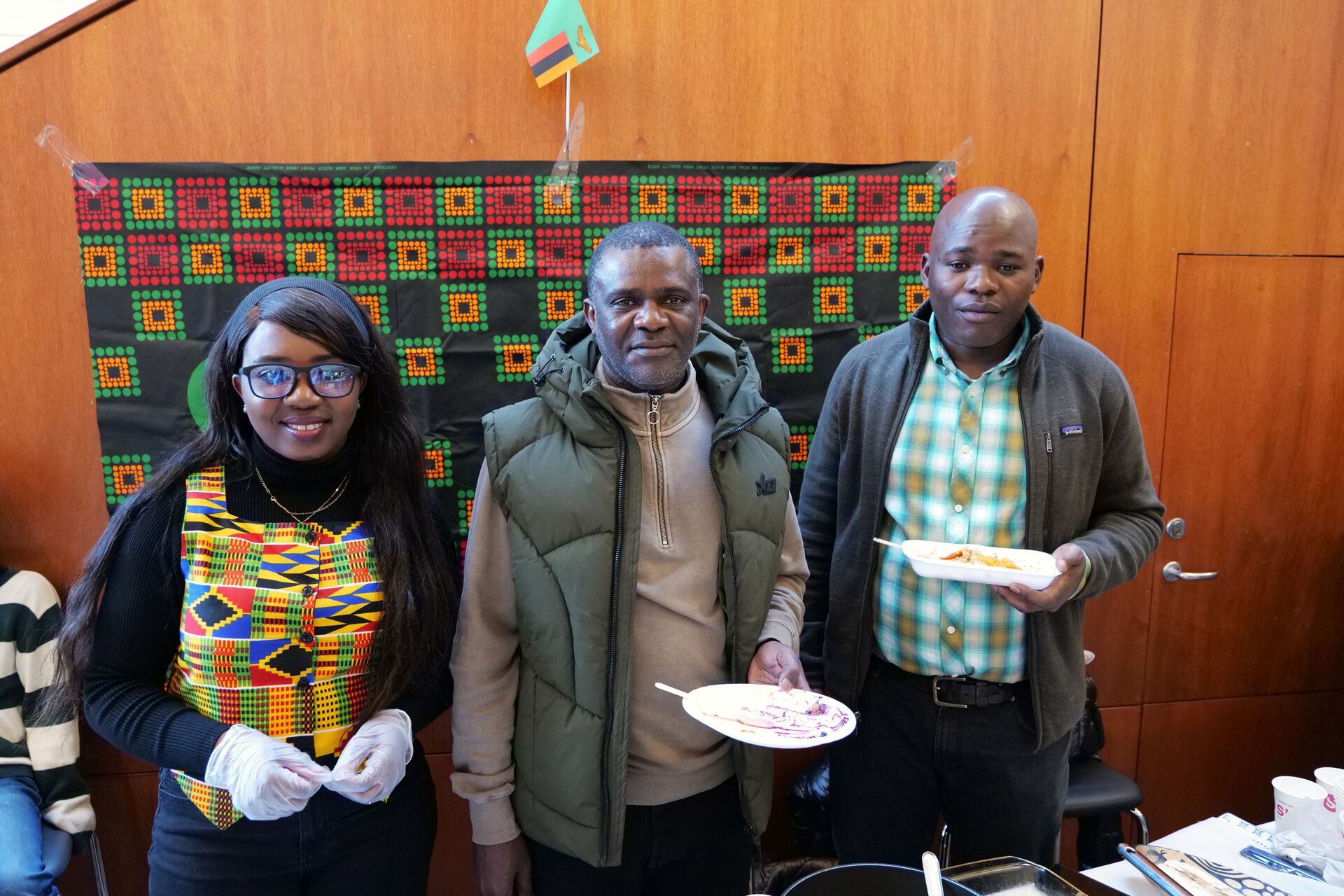 A woman and two men are holding plates of food