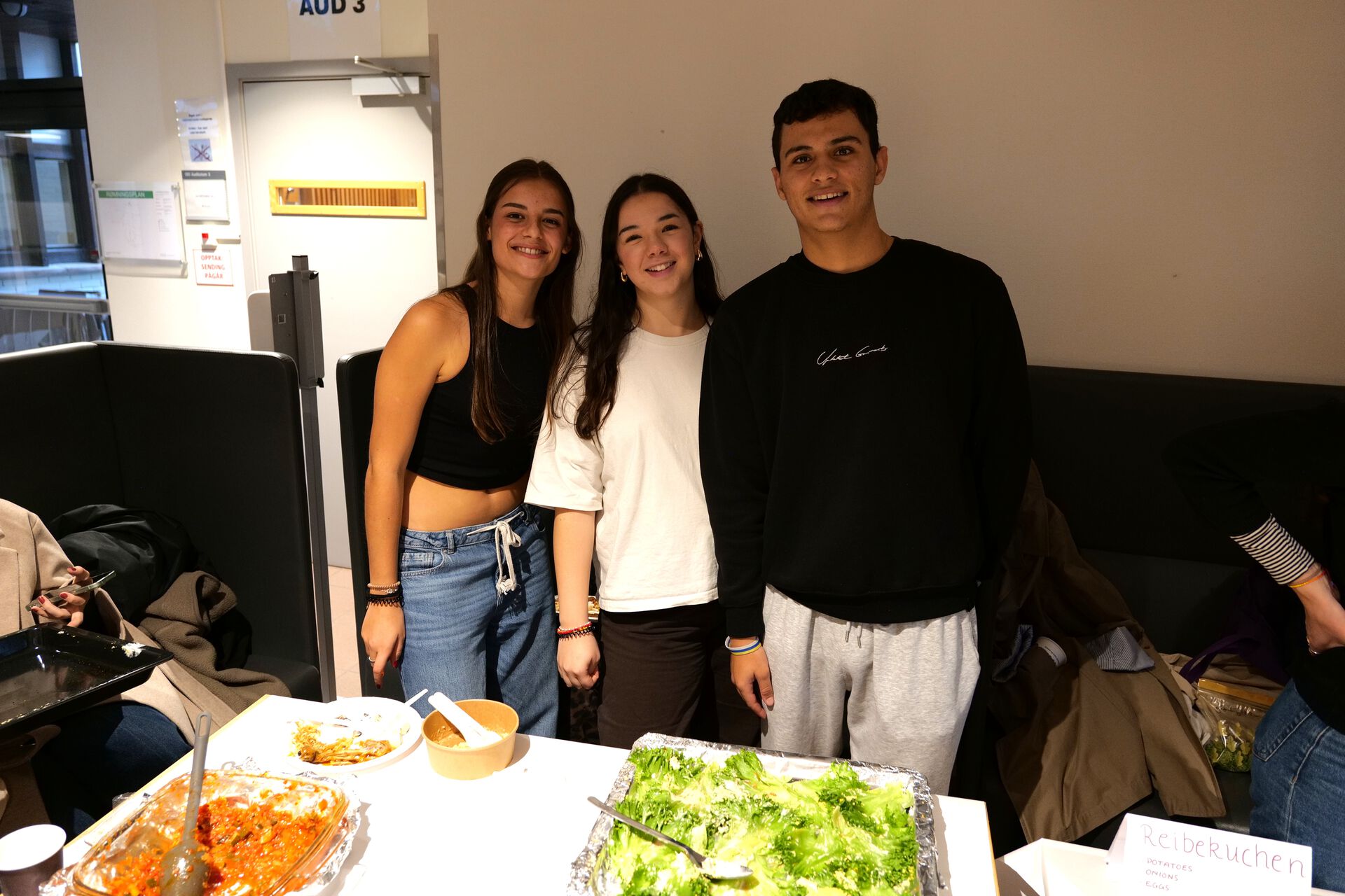 Three students are smiling by a table