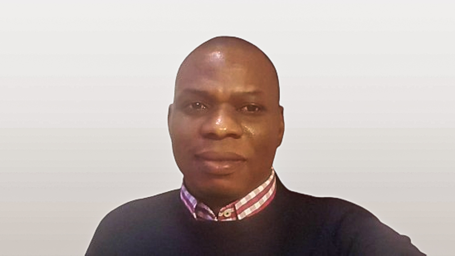 Black man against a whiote wall with shirt and jumper 