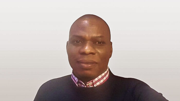 Black man against a whiote wall with shirt and jumper 