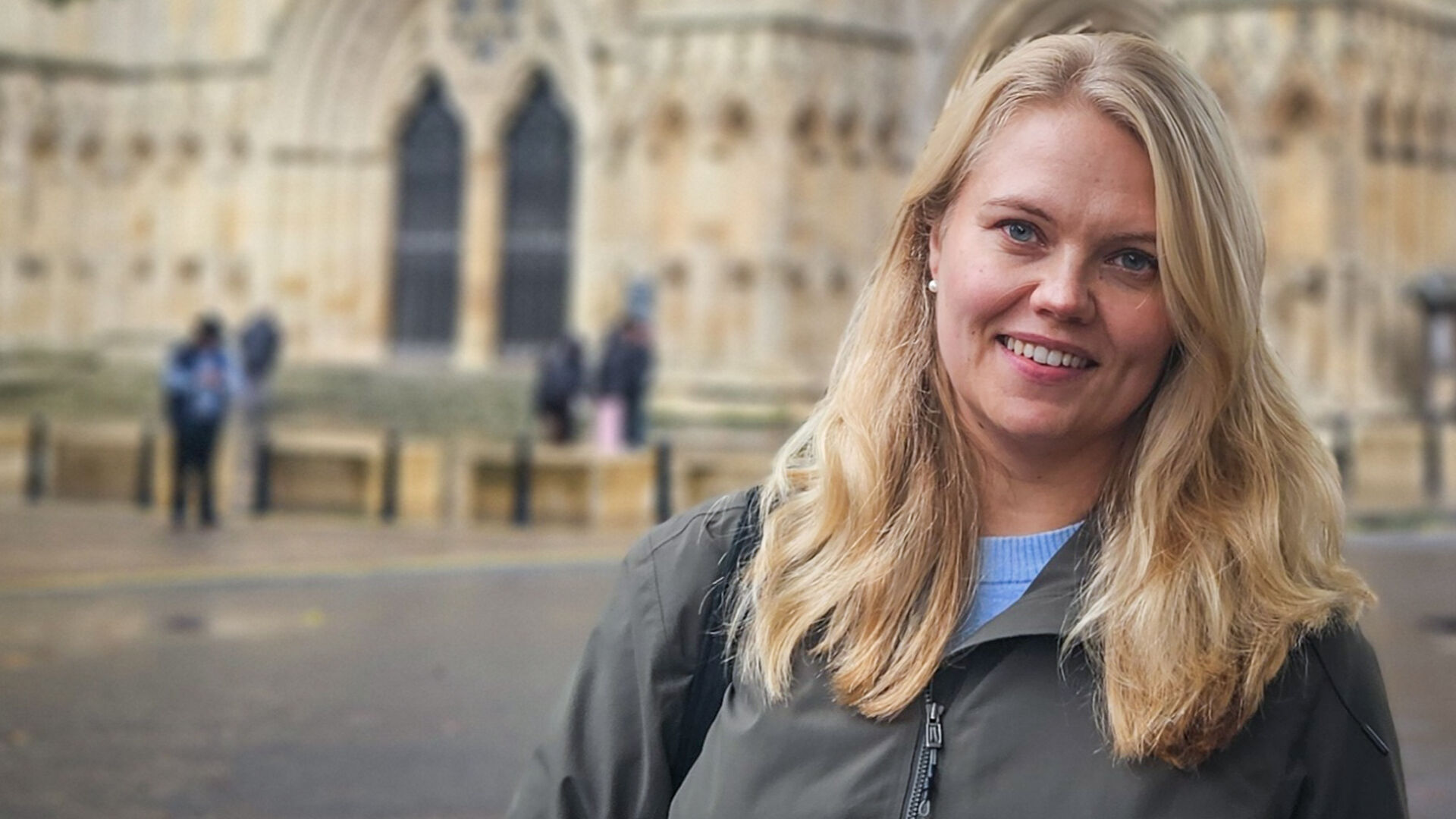 Woman with blonde hair in front of a old stonechurch