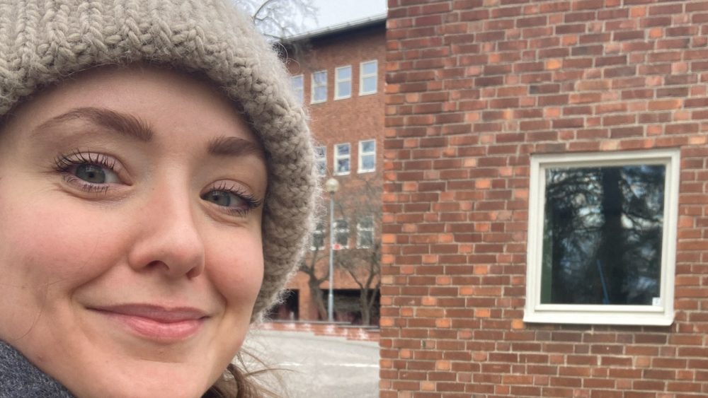 Photo of Beate wearing a winter hat in front of a brick building 