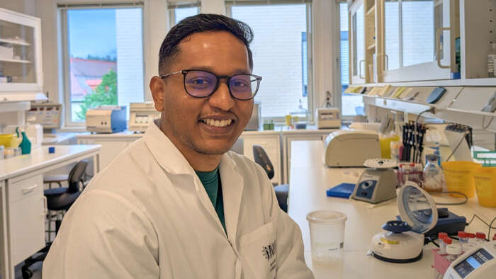 A smiling man wearing glasses and a white lab coat in a laboratory. 