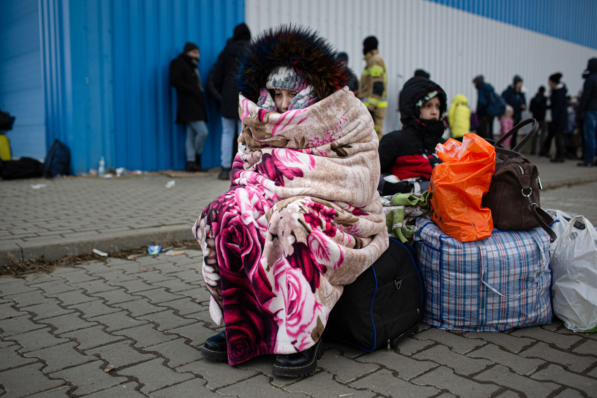 A woman covered in a blanket with her belongings beside her. 