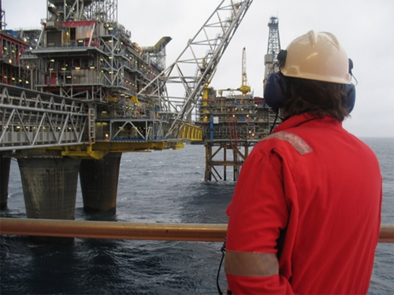 man i orange suit and white helmet in front of oil plattform Oseberg in Norway