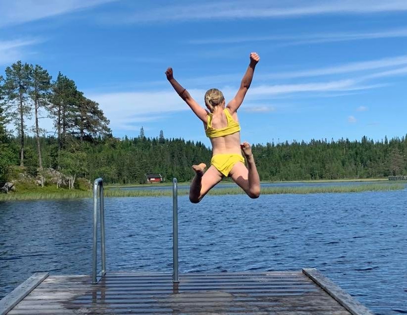 girl in yellow bikini jumping in front of blue sky into a lake