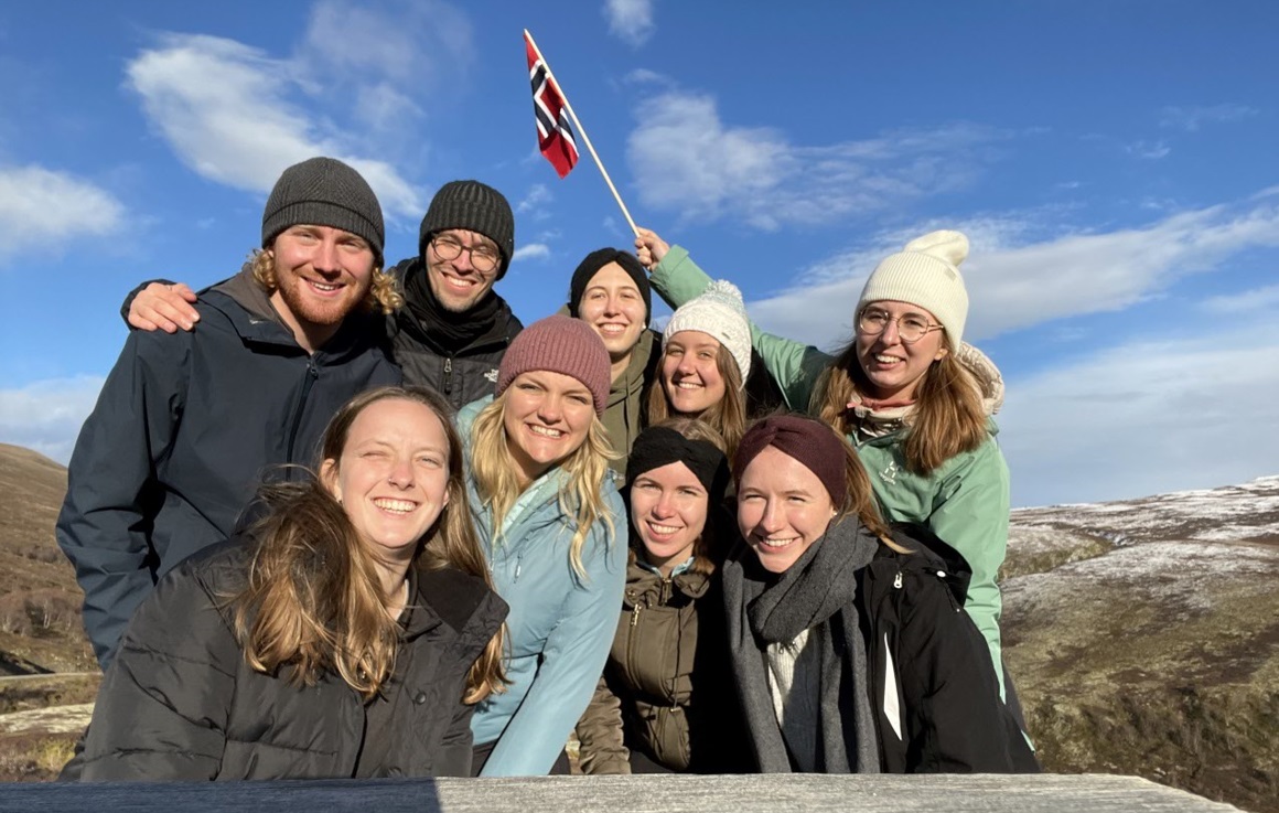 Several exchange students on a roadtrip outdoors, waving the Norwegian flag