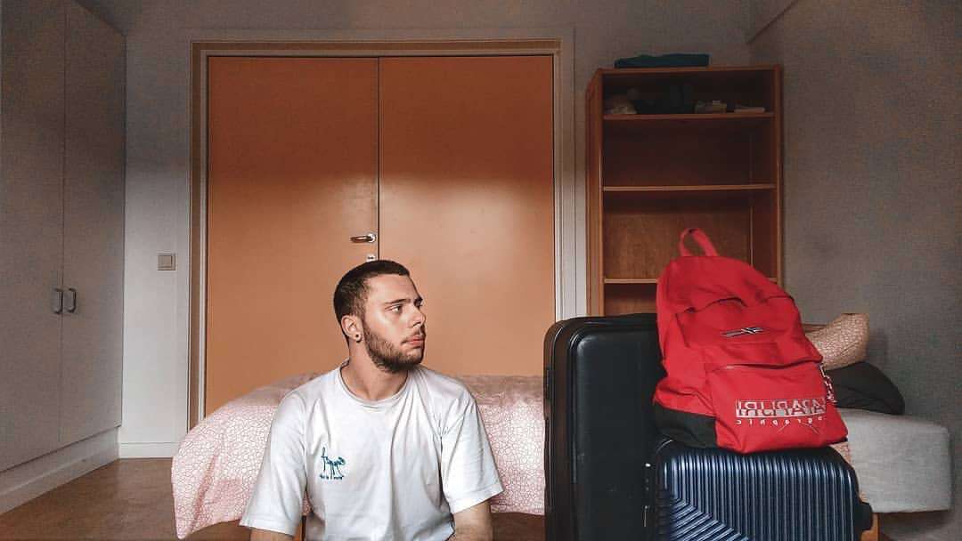A male student is sitting in his room after packing his suitcases, looking sad, ready to go back home after his exchange.