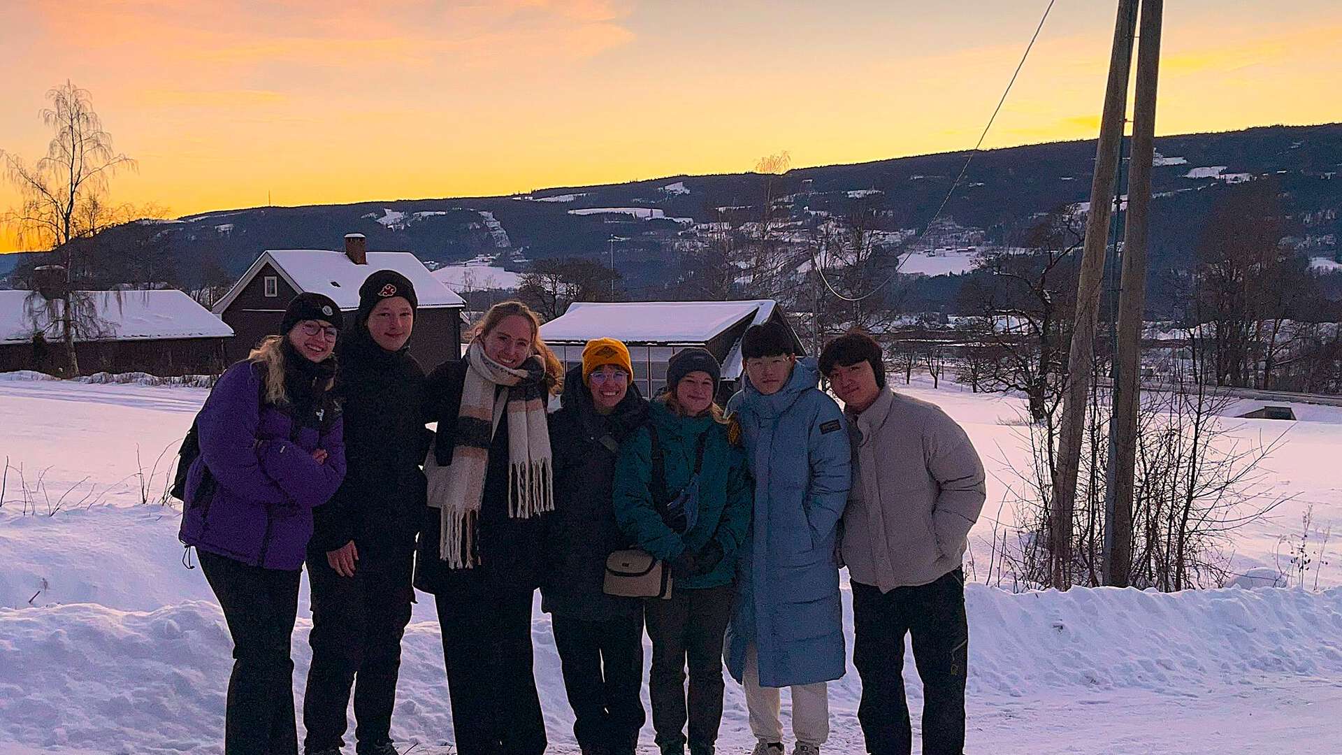 Exchange students happily posing together for the camera with a beautiful winter sunset in the back.